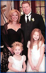 The image features a family posing together at a formal event the father is wearing a tuxedo, the mother is dressed in evening wear, and there are three children in formal attire.