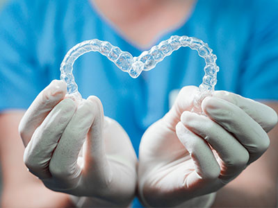 A dental professional s hands holding a transparent heart-shaped object with clear braces inside, symbolizing love for orthodontics.